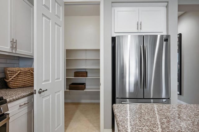 kitchen with backsplash, white cabinetry, light stone countertops, light tile patterned floors, and stainless steel fridge