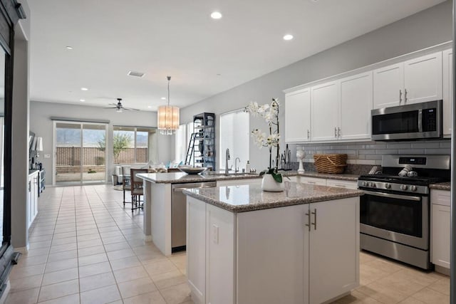 kitchen featuring pendant lighting, appliances with stainless steel finishes, a kitchen island, kitchen peninsula, and light stone counters