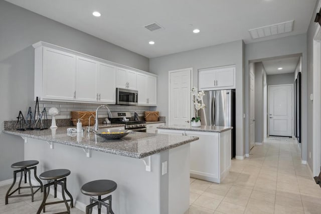 kitchen featuring light stone countertops, white cabinetry, stainless steel appliances, backsplash, and kitchen peninsula