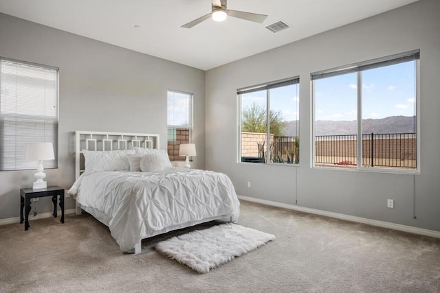 bedroom featuring ceiling fan, light colored carpet, a mountain view, and multiple windows