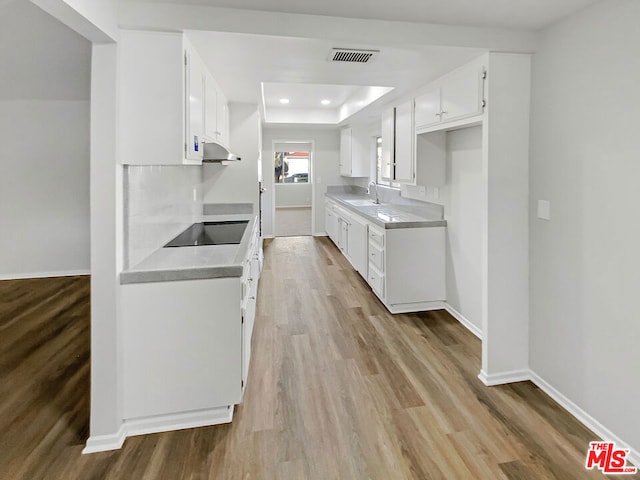 kitchen featuring sink, light hardwood / wood-style flooring, a tray ceiling, black electric stovetop, and white cabinets