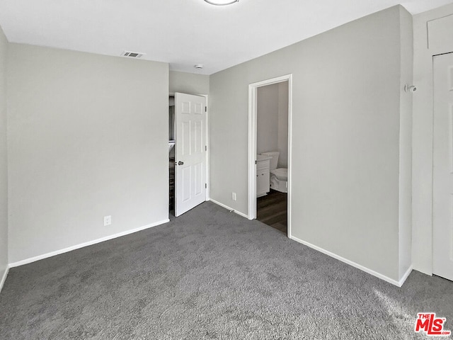 unfurnished bedroom featuring ensuite bathroom and dark carpet