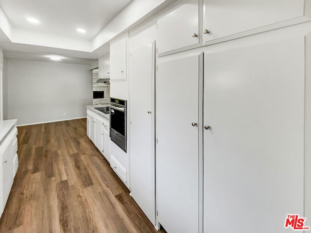 kitchen featuring a stone fireplace, hardwood / wood-style floors, white cabinetry, decorative backsplash, and stainless steel oven