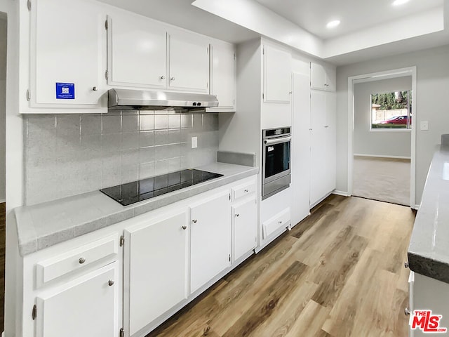 kitchen with white cabinetry, oven, decorative backsplash, black electric stovetop, and light hardwood / wood-style floors