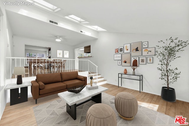 living room featuring vaulted ceiling with skylight, ceiling fan, and light wood-type flooring