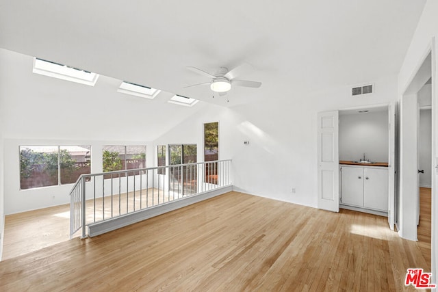 unfurnished living room with ceiling fan, sink, a healthy amount of sunlight, lofted ceiling with skylight, and light hardwood / wood-style floors