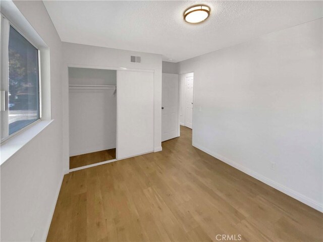 unfurnished bedroom featuring wood-type flooring, a closet, and a textured ceiling