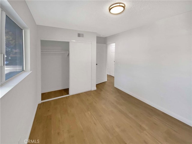 unfurnished bedroom featuring a textured ceiling, visible vents, wood finished floors, baseboards, and a closet