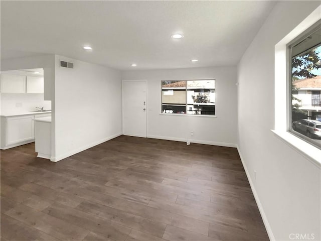 unfurnished living room featuring dark wood-type flooring, sink, and a healthy amount of sunlight