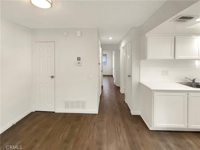 corridor featuring baseboards, visible vents, dark wood-style floors, and a sink