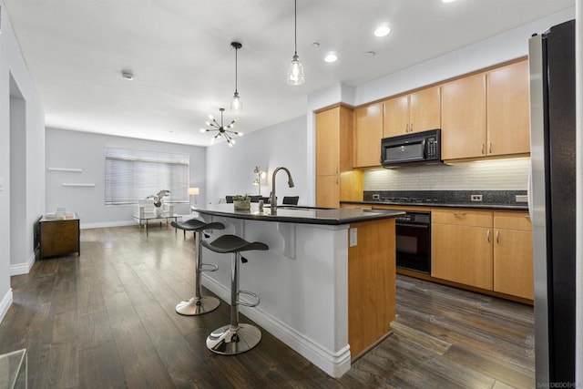 kitchen featuring an island with sink, decorative light fixtures, dark hardwood / wood-style flooring, black appliances, and sink