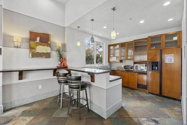 kitchen with pendant lighting, paneled built in fridge, decorative backsplash, kitchen peninsula, and a breakfast bar area