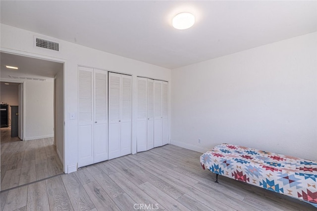 unfurnished bedroom with light hardwood / wood-style flooring and multiple closets