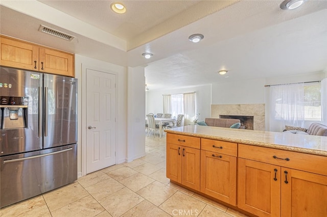 kitchen featuring light tile patterned floors, light stone countertops, stainless steel fridge with ice dispenser, and a textured ceiling