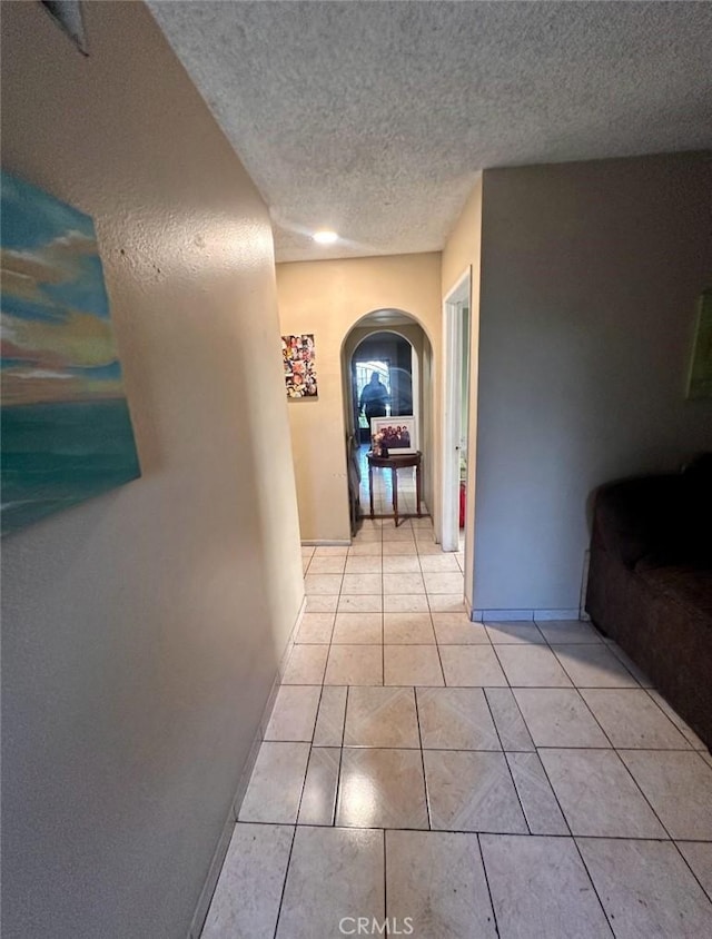 hallway with a textured ceiling and light tile patterned floors