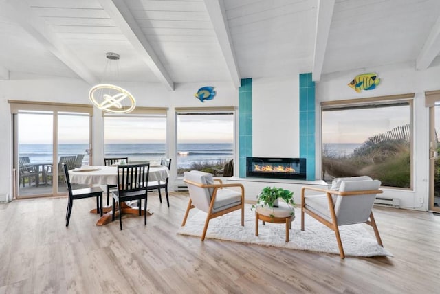 sunroom with a water view, a notable chandelier, baseboard heating, a fireplace, and beam ceiling