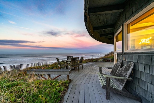 deck at dusk with a water view and a view of the beach