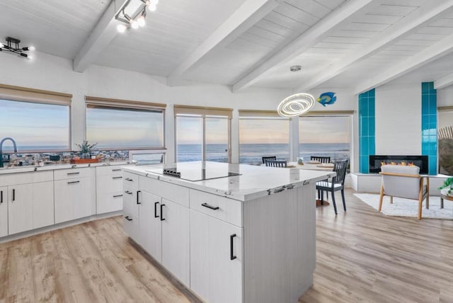 kitchen featuring white cabinetry, beamed ceiling, a water view, a tile fireplace, and black electric cooktop