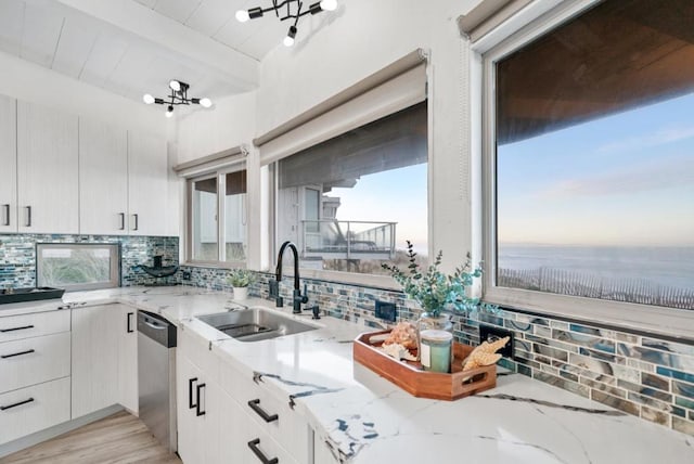 kitchen featuring light stone countertops, sink, stainless steel dishwasher, and beam ceiling