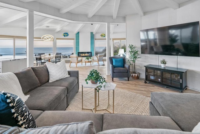 living room with a large fireplace, light hardwood / wood-style flooring, beam ceiling, and a water view