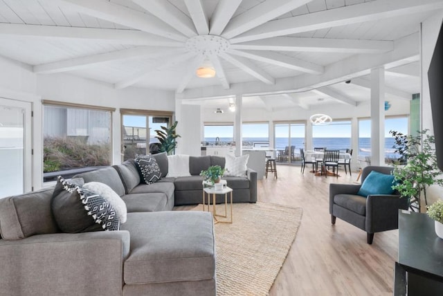 living room featuring beamed ceiling, light hardwood / wood-style flooring, a water view, and an inviting chandelier