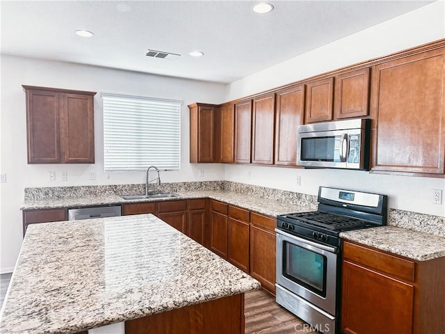 kitchen featuring stainless steel appliances, dark hardwood / wood-style floors, sink, light stone counters, and a center island