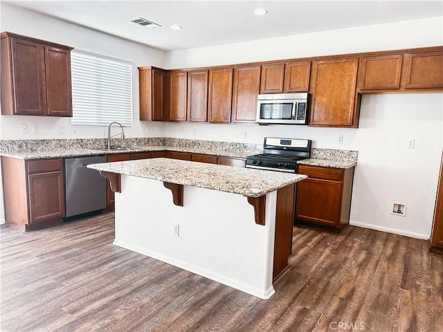 kitchen with a breakfast bar area, stainless steel appliances, light stone countertops, a kitchen island, and sink