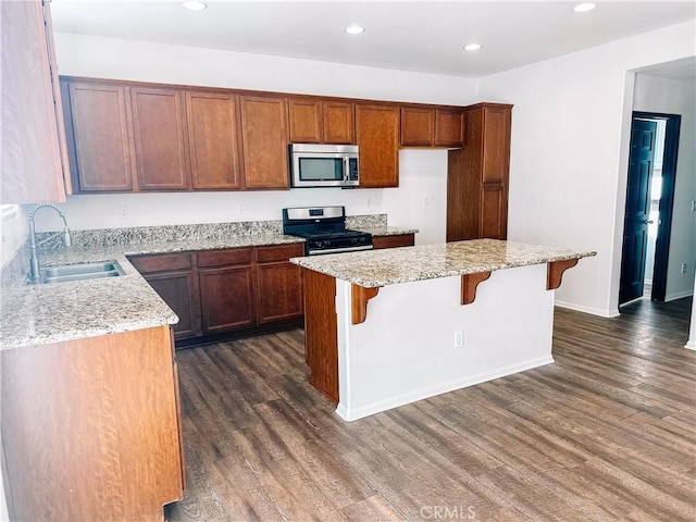 kitchen featuring a breakfast bar area, appliances with stainless steel finishes, a center island, light stone counters, and sink