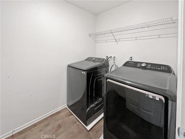 laundry area with laundry area, washing machine and dryer, baseboards, and wood finished floors