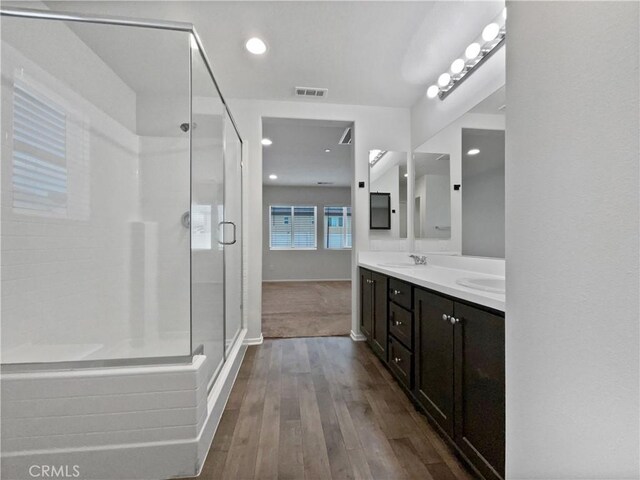 full bathroom with wood finished floors, a sink, visible vents, double vanity, and a stall shower