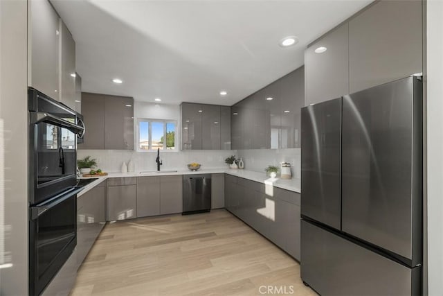 kitchen with appliances with stainless steel finishes, tasteful backsplash, light hardwood / wood-style floors, sink, and gray cabinets