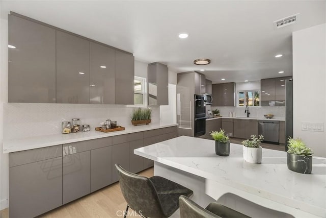 kitchen featuring gray cabinets, light hardwood / wood-style floors, a breakfast bar, sink, and appliances with stainless steel finishes