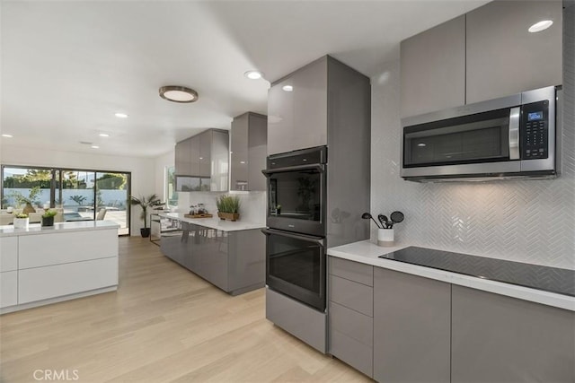 kitchen with light hardwood / wood-style floors, backsplash, gray cabinets, and stainless steel appliances