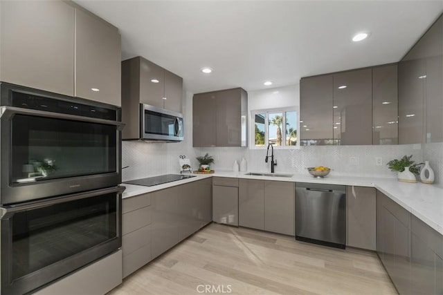 kitchen featuring appliances with stainless steel finishes, gray cabinetry, backsplash, light wood-type flooring, and sink