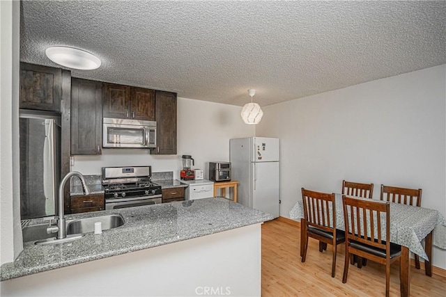 kitchen with appliances with stainless steel finishes, light hardwood / wood-style floors, sink, light stone counters, and dark brown cabinets