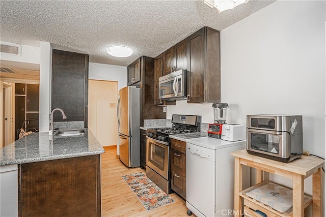 kitchen featuring appliances with stainless steel finishes, a textured ceiling, stone counters, light hardwood / wood-style flooring, and sink