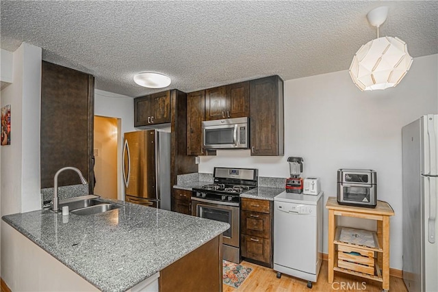 kitchen featuring kitchen peninsula, stainless steel appliances, dark stone countertops, light hardwood / wood-style flooring, and sink