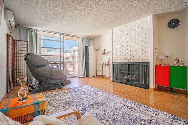 living room featuring a wall mounted AC, wood-type flooring, a brick fireplace, and a textured ceiling