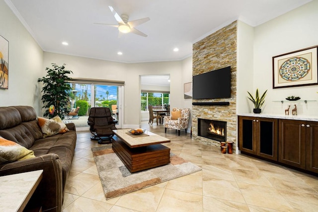 living room featuring ceiling fan, crown molding, and a stone fireplace