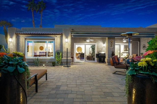 back house at night featuring ceiling fan and a patio