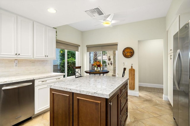 kitchen with ceiling fan, stainless steel appliances, decorative backsplash, a kitchen island, and white cabinets