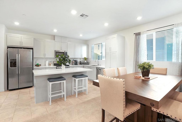 kitchen featuring white cabinets, stainless steel appliances, a center island, and a kitchen bar