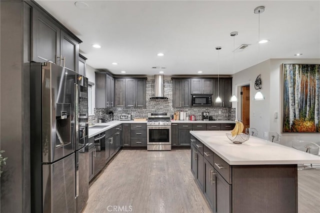 kitchen with stainless steel appliances, tasteful backsplash, decorative light fixtures, light wood-type flooring, and wall chimney range hood