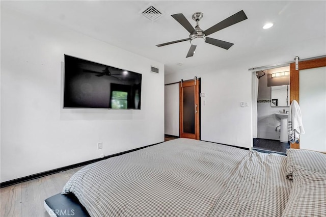 unfurnished bedroom with ceiling fan, a barn door, and light wood-type flooring