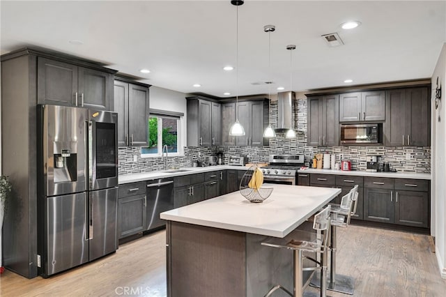 kitchen featuring appliances with stainless steel finishes, wall chimney exhaust hood, light hardwood / wood-style floors, and decorative light fixtures