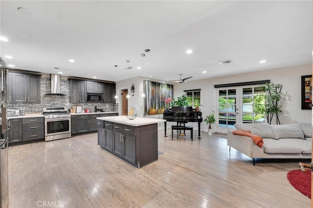 kitchen featuring decorative backsplash, built in microwave, stainless steel range oven, an island with sink, and wall chimney exhaust hood