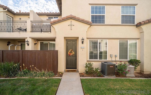 entrance to property with a balcony, cooling unit, and a lawn