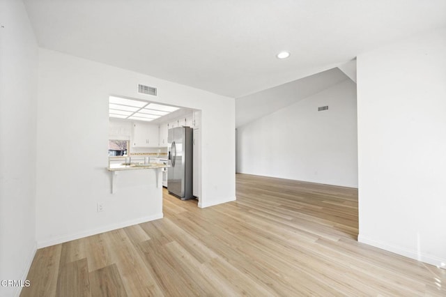 unfurnished living room with sink, light hardwood / wood-style flooring, and vaulted ceiling