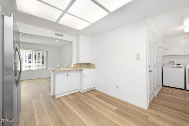 kitchen with kitchen peninsula, white cabinets, stainless steel refrigerator, washing machine and dryer, and light hardwood / wood-style flooring