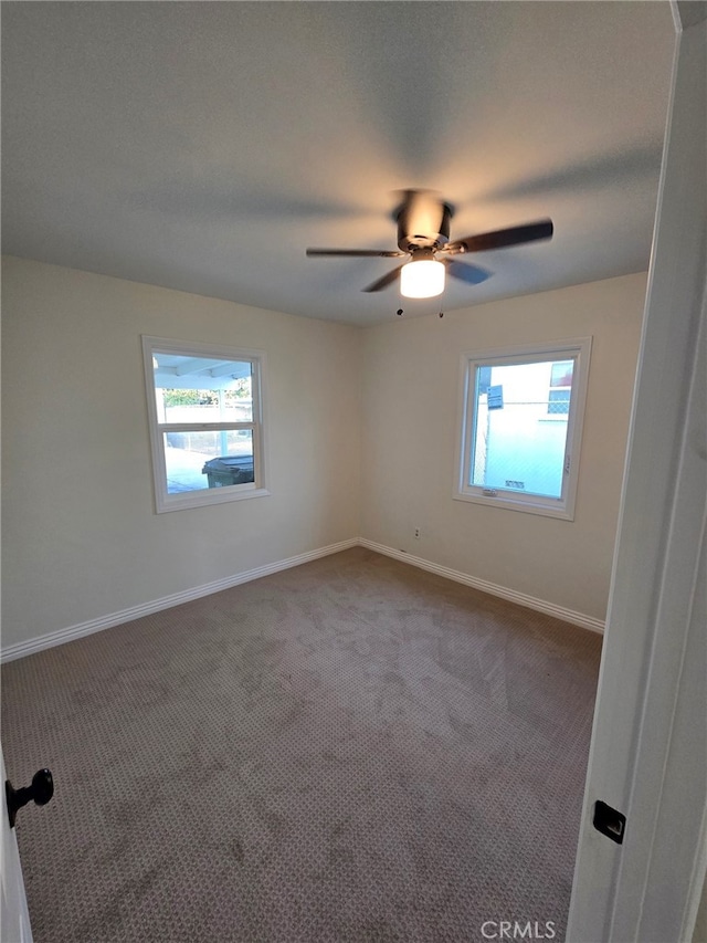 carpeted spare room featuring ceiling fan and a wealth of natural light